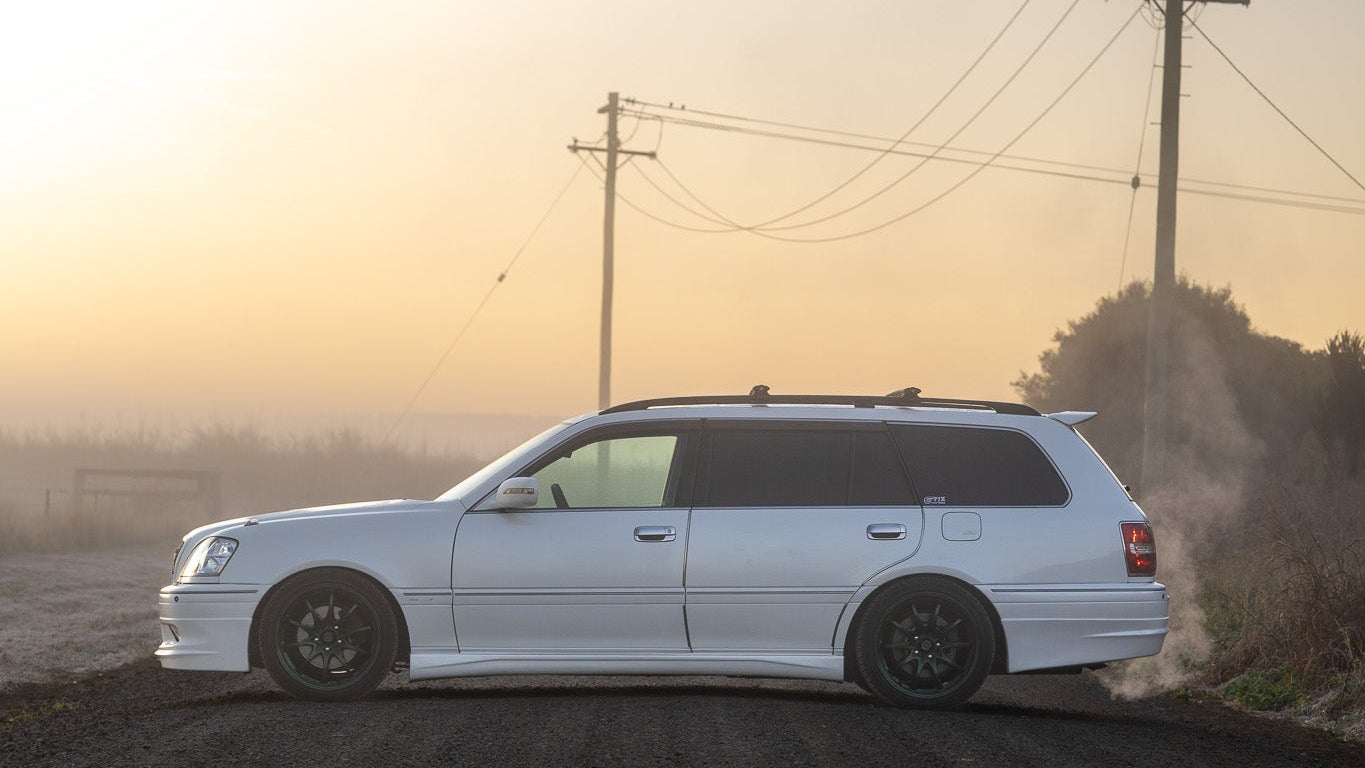 White station wagon on a dirt road with power lines and sunset in the background